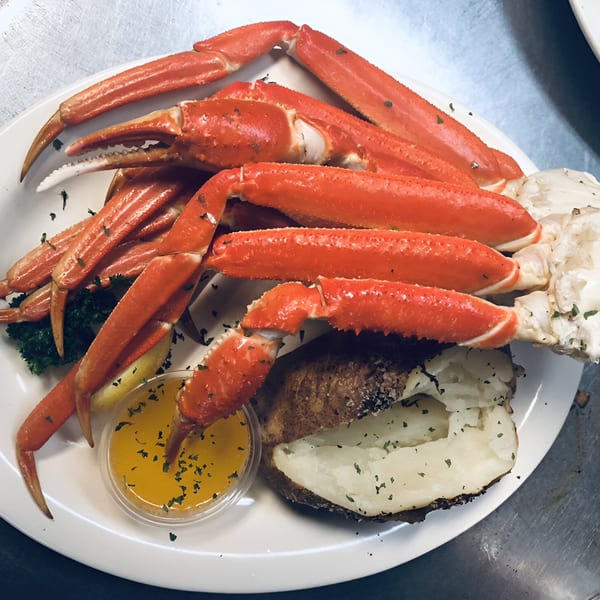 A plate of bright red crab legs, a baked potato, lemon, and melted butter with herbs.