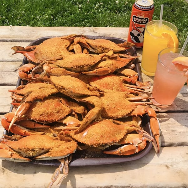 Steamed crabs seasoned with Old Bay, a National Bohemian beer, and cocktails on a wooden table.
